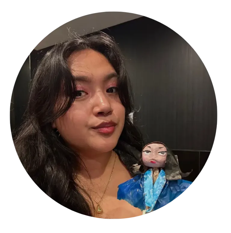 Portrait of Chastidy, a woman with black hair holding a paper mache doll of herself